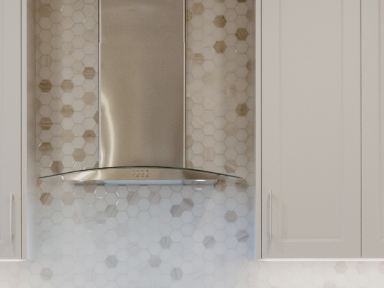 Sleek glass and stainless steel chimney -style hood fan, backed by hexagonal tile to the ceiling.